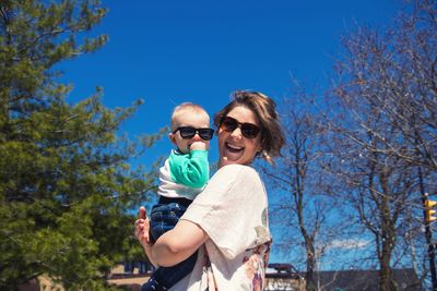 Portrait of smiling mother and son in sunglasses against sky