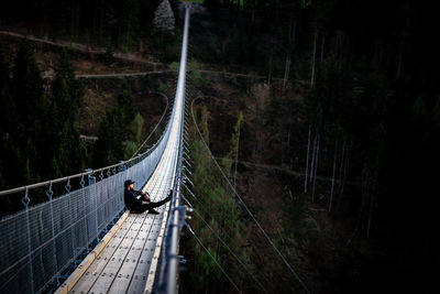 Man sitting on footbridge in forest