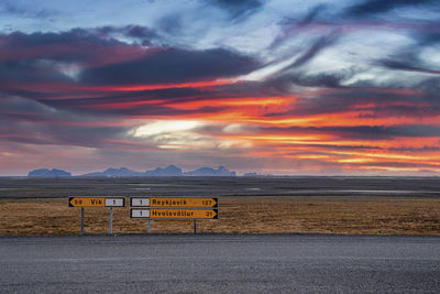 Signboards by road on volcanic landscape against dramatic sky during sunset