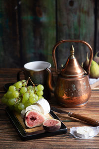 Cheese plate with goat cheese, grapes and figs, copper teapot, angle view