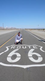 Full length of man crouching on road against clear blue sky