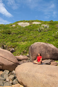 Man sitting on rock by mountain against sky