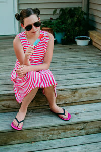 Full length of woman wearing sunglasses sitting on wood