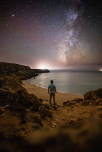 Rear view of man standing at beach against star field