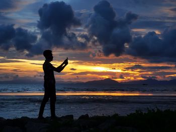 Silhouette man standing on beach against sky during sunset