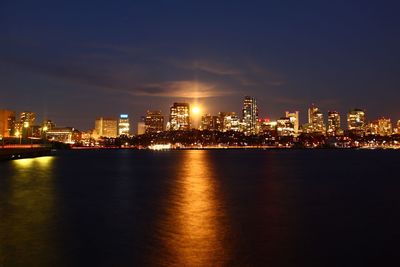Illuminated city by sea against sky at night