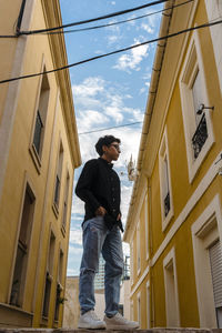 Young transgender man posing outdoors in the narrow street of a town.