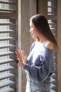 Side view of young woman standing against window