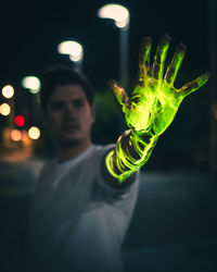 Young man showing green glowing hand at night