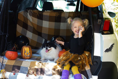 Portrait of cute girl sitting with dog in car trunk