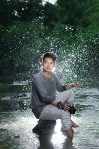 Young man sitting on rock in river while looking away