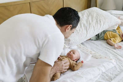 Smiling man playing with baby on bed at home