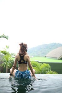 Rear view of woman sitting on infinity pool against sky