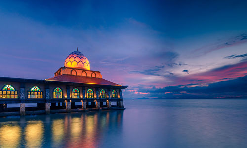 Illuminated mosque by sea at dusk