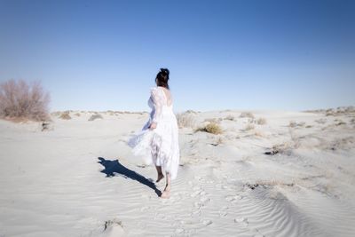 Full length of bride walking on desert against sky