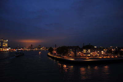 Illuminated buildings by river in city against sky