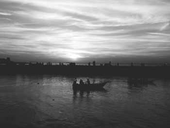 Silhouette people on water against sky at sunset