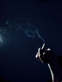 Cropped hand of person holding burning cigarette in darkroom