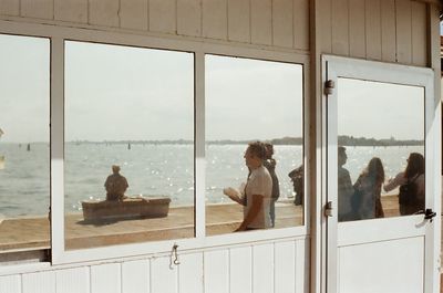 People looking at sea seen through glass window