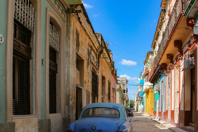 Old car on street amidst buildings against blue sky