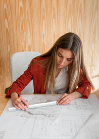 Young and beautiful woman working in architectural project with wood wall behind