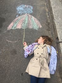 High angle view of girl lying by drawn umbrella on footpath