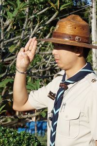 Close-up of man in hat gesturing while standing by plants