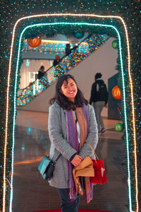 Portrait of smiling woman standing against illuminated christmas wall