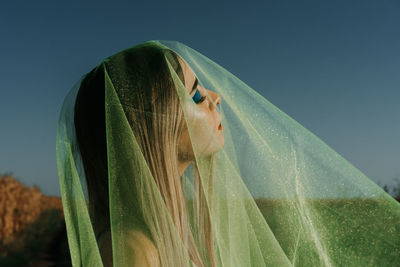 Close-up of young woman covered with scarf against clear sky