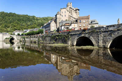 Arch bridge over lake by buildings against sky