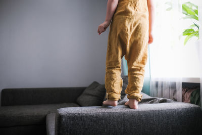 Child jumps and plays on sofa in minimalist living room, gray sofa.