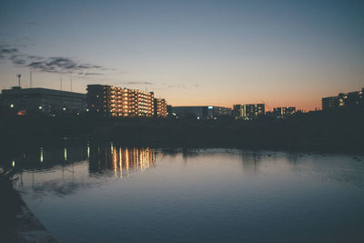 Buildings by river against sky at sunset