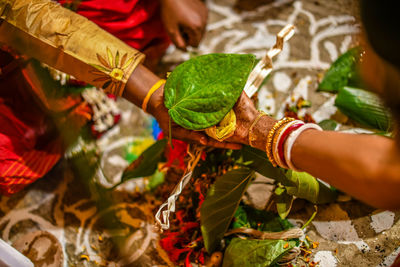 Cropped image of bride with groom holding leaf during wedding