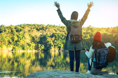 Rear view of man and woman standing by lake against clear sky