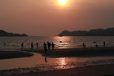 Silhouette people on beach against sky during sunset