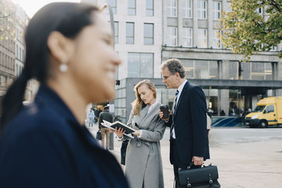 Business coworkers looking in book while standing in city