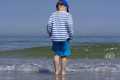 Rear view of man standing on beach against clear sky