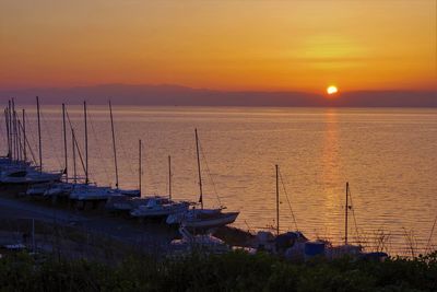 Sailboats moored in sea against sky during sunset