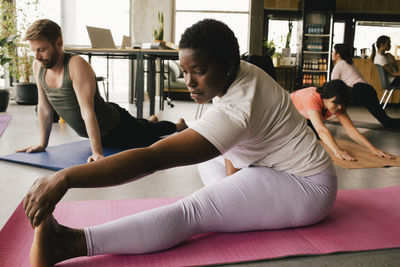 Flexible businesswoman practicing yoga near businessman on exercise mats at office