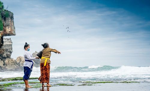 Rear view of man and woman on sea shore against sky