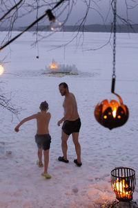 Shirtless father and son walking together on snow during dusk