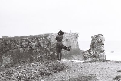 Rear view of man looking at rock against clear sky