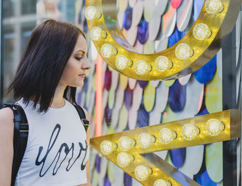 Young woman looking at window standing by store in city