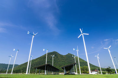 Low angle view of wind turbines on field against blue sky