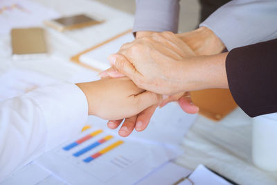 Cropped image of colleagues with stacked hands over desk