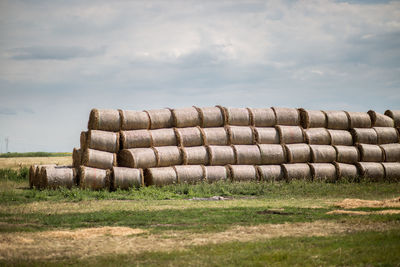 Stacked hay bales with coverings on field against cloudy sky