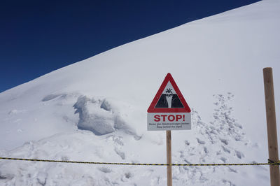 Road sign on snow covered landscape against clear sky