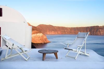 Deck chairs on table by sea against clear sky