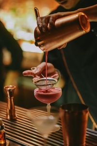 Midsection of bartender pouring cocktail in glass