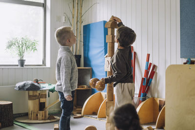 Boy stacking toy blocks while male friend looking at him in day care center